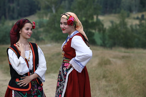 A group of dancers different age are dressed in paired (female and male) Belarusian, Georgian and Moldavian traditional clothes. They are posing together, smiling looking at the camera. Studio shooting