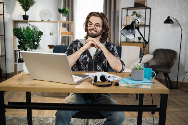 istock Man in checkered shirt and eyeglasses sitting at table with modern laptop. 1414451432