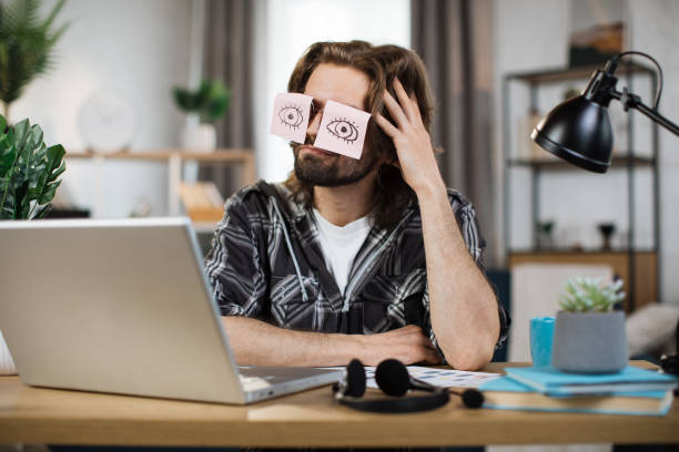 istock Tired caucasian male student sleeping with stickers on eyes, sitting at table 1414451503