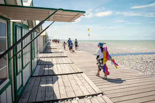 girl walking with inflatable unicorn in front of colorful wooden beach huts in France at pebble beach in Cayeux-sur-Mer, France