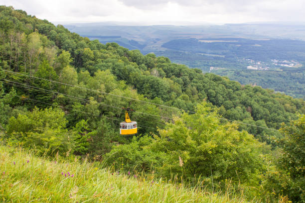 the cab of the funicular rises on a cable rope against the background of a wooded mountain slope A beautiful landscape - the cab of the funicular rises on a cable rope against the background of a wooded mountain slope and a valley in a haze to the horizon on a summer day and a copy space blurred motion street car green stock pictures, royalty-free photos & images