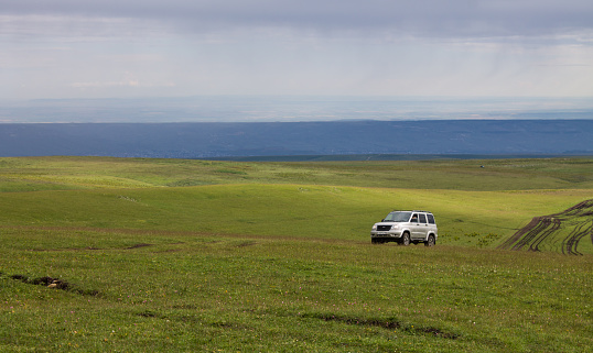 Karachay-Cherkessia: An SUV car rides off-road on a green hilly field on a cloudy summer day and a space for copying