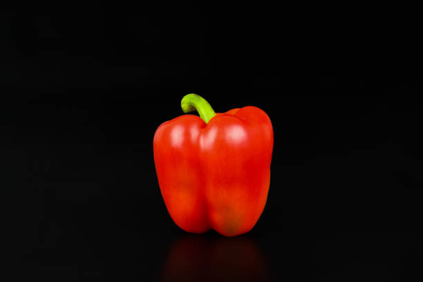 Green and red well ripened bell peppers in clay plate on wooden table. View from above.