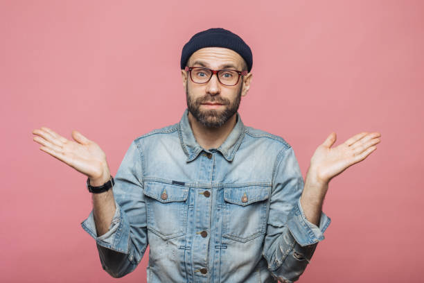 photo of attractive bearded male wears fashionable clothing, shrugs shoulders in bewilderment, makes serious decision, isolated over pink background. confused hesitant unshaven stylish man - bolero jacket imagens e fotografias de stock