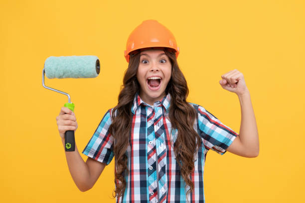 istock surprised kid with curly hair in construction helmet hold paint roller, decoration 1414465098