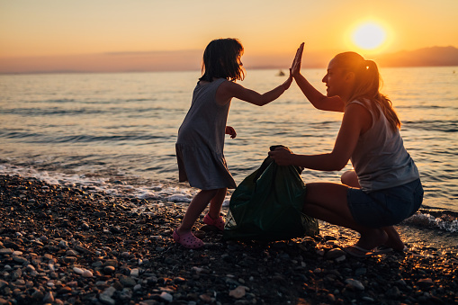 After successfully cleaning the beach of trash, mother and daughter high-five each other