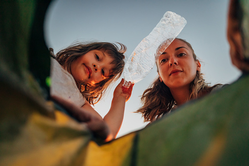 Una mujer y una niña arrojan botellas de plástico a una bolsa de plástico photo