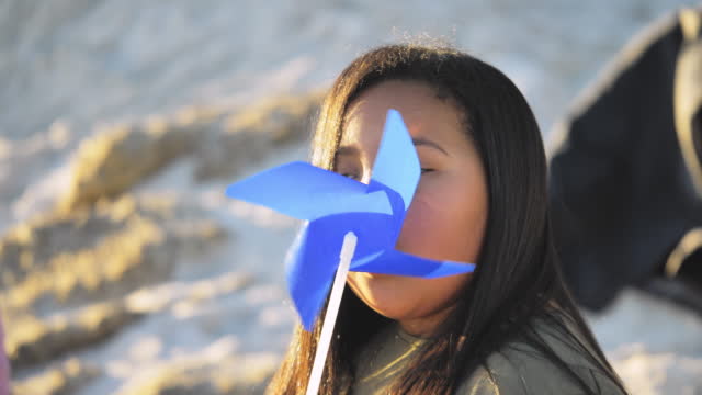 Close up portrait girl blowing blue pinwheel on beach