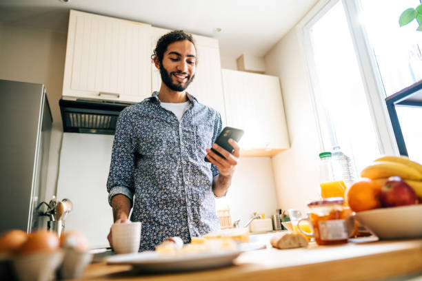 istock Multiracial millennial man having breakfast in modern kitchen and using smart phone 1414471022