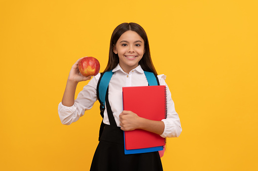 Happy kid go back to school holding apple and books yellow background, knowledge day.