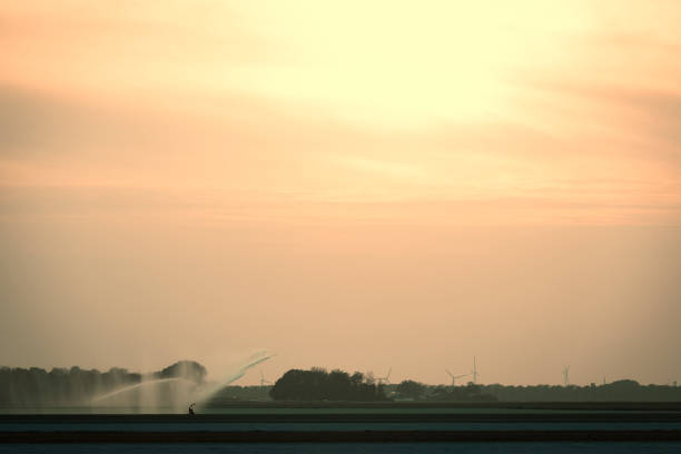 Irrigation pivot gun machine spraying water on a field during a dry and warm spring day in the Noordoostpolder, Flevoland, Netherlands. Over the last years there have been longer periods of draught causing problems for farmers cultivating crops.