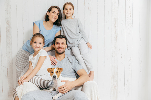 Portrait of happy family indoor. Handsome father holds dog, beautiful brunette mother and two daughters, have fun together, pose for family album, spend time together. People, relationships concept