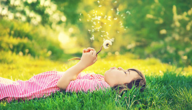 istock Close-Up Of Girl Blowing Dandelion Seed While Lying On Grass 1414479238