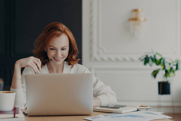 istock Positive happy female freelancer has busy working day, works distantly from home, sits in front of laptop computer against modern interior, works on creative task, watches webinar for improving skills 1414481349