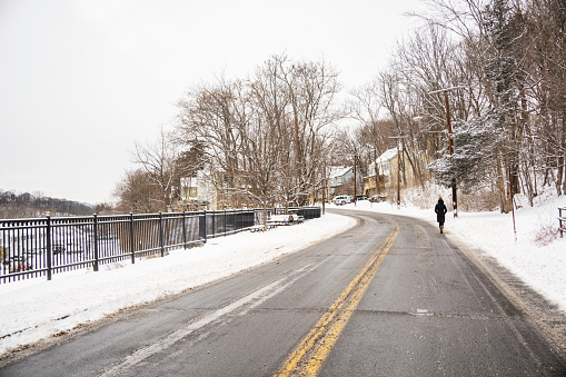 Rear view of a woman walking down a snow covered road in a small town on a overcast day in winter