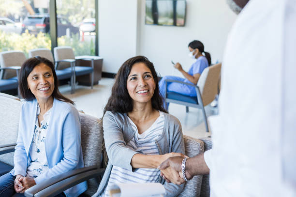 mother watches as her daughter shakes hands - doctor patient greeting talking imagens e fotografias de stock