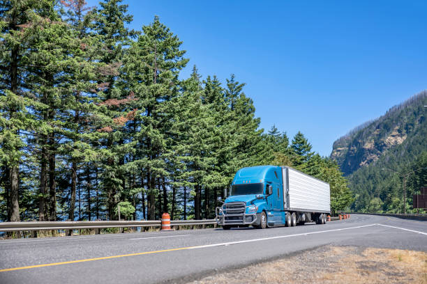 istock Light blue big rig semi truck with grille guard transporting cargo in refrigerator semi trailer driving on highway road with fork divided traffic lines 1414481896