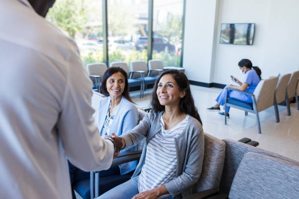 mid adult female patient smiles as she shakes the doctor's hand - doctor patient greeting talking imagens e fotografias de stock