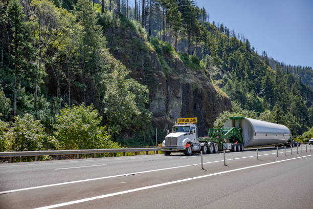 potente tractor de camión de plataforma grande con señal de carga de gran tamaño que transporta una construcción industrial larga de gran tamaño en un semirremolque especializado con carro de montaje adicional que funciona en la carretera - run of the mill fotografías e imágenes de stock