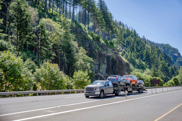 Compact truck transporting cars on the small semi trailer running on the scenic highway road with forest and mountain stock photo