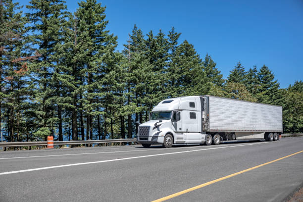 istock Comfortable pro white big rig semi truck transporting cargo in reefer semi trailer driving on the multiline highway road 1414483356