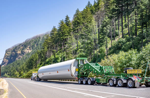 semirremolque de plataforma grande de servicio pesado que transporta parte del poste del generador de molino de viento de gran tamaño largo en el semirremolque especializado con carros adicionales y letrero de carga de gran tamaño en la parte posterior - run of the mill fotografías e imágenes de stock