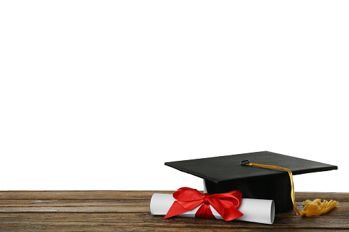 Graduation hat and diploma on wooden table against  white background, space for text