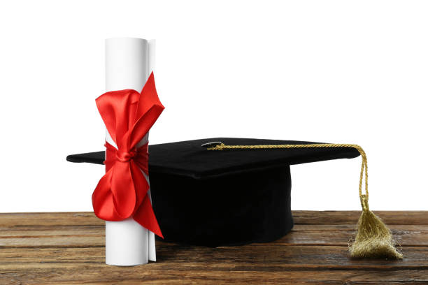istock Graduation hat and diploma on wooden table against  white background 1414484904