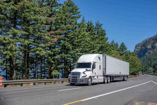 istock Popular pro big rig white semi truck with chrome grille guard transporting cargo in refrigerated semi trailer driving on the divided highway road 1414485539