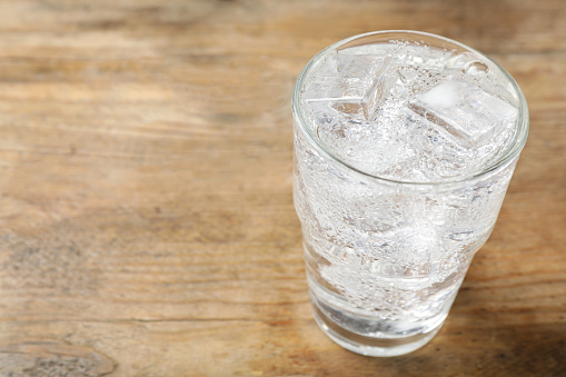 Glass of soda water with ice on wooden table. Space for text