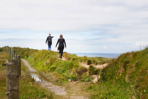 Rear view of a two women hiking along a narrow pathway in high mountains and looking at the view