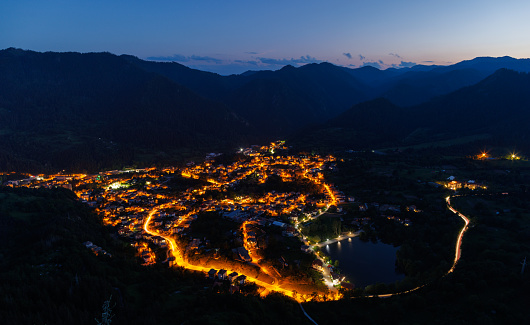 Bright sparkling mountain town of Smolyan with multi-colored night electric lights, against the backdrop of the mountain range of the Rhodope Mountains and the evening dark cloudy sky