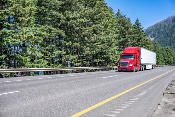 istock Red big rig semi truck with truck driver sleeping compartment transporting cargo in dry van semi trailer running long haul freight on the highway road with forest and mountain in Oregon 1414486175