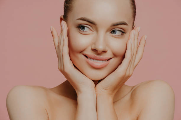 face lift, skin care and wellness concept. headshot of charming caucasian young woman touches cheeks gently, has glowing hydrated skin, has bare soulders, looks tenderly aside. beauty portrait. - lifting device imagens e fotografias de stock