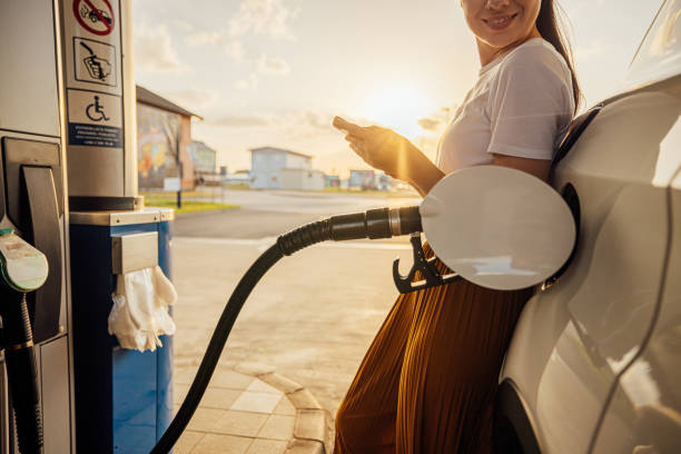 istock Young woman using mobile phone while refueling her car at gas station 1414488291