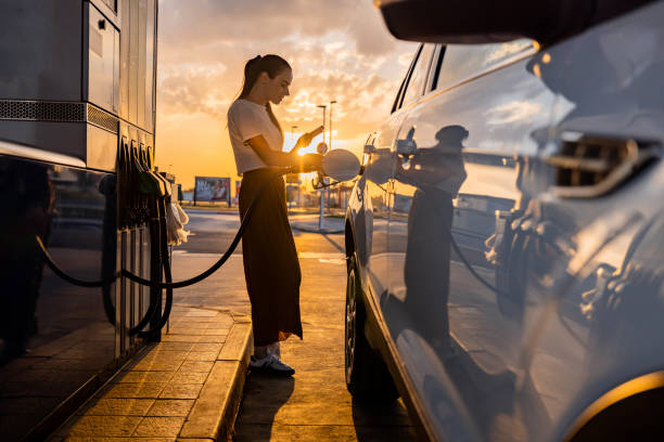 istock Young woman using mobile phone while refueling her car at gas station 1414488531