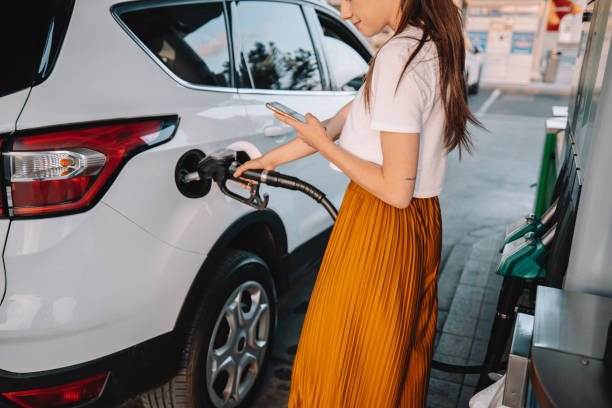 istock Young woman using mobile phone while refueling her car at gas station 1414488532