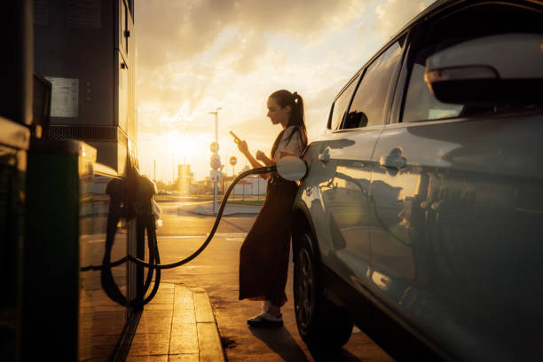 istock Young woman using mobile phone while refueling her car at gas station 1414488533