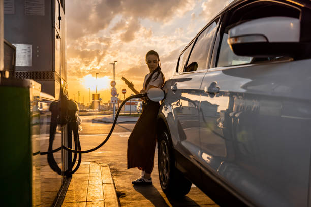 istock Young woman using mobile phone while refueling her car at gas station 1414488582