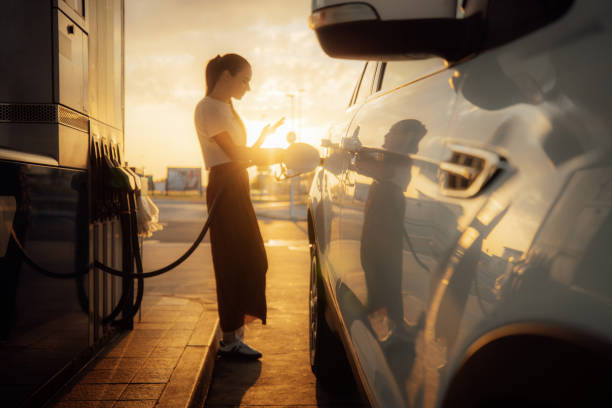istock Young woman using mobile phone while refueling her car at gas station 1414488630