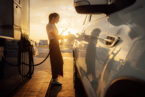 Young woman using mobile phone while refueling her car at gas station stock photo