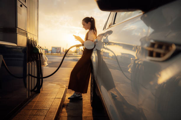 istock Young woman using mobile phone while refueling her car at gas station 1414488656