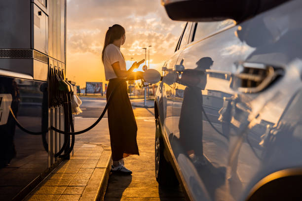 istock Young woman using mobile phone while refueling her car at gas station 1414488735