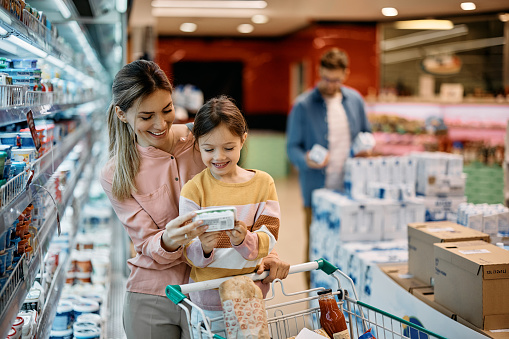 Happy mother and daughter reading nutrition label while buying diary product in supermarket.