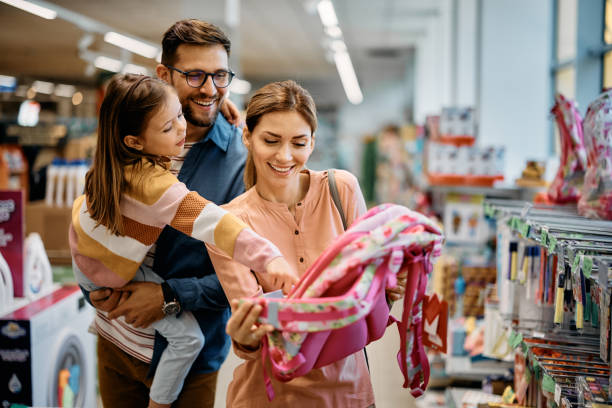 happy little girl pointing at backpack while buying school supplies with her parents in supermarket. - koopwaar stockfoto's en -beelden