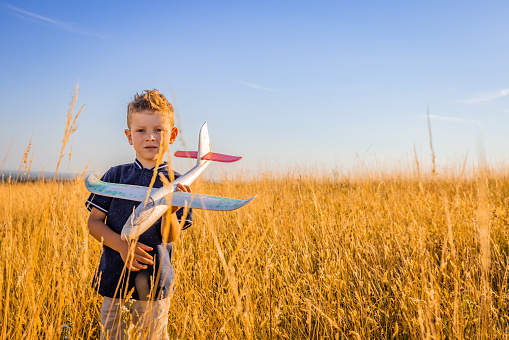 Portrait of boy playing with toy while standing amidst grassy field against sky during golden hour
