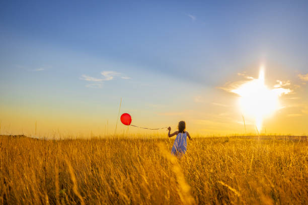 fille jouant avec un ballon tout en courant au milieu de l’herbe dans la prairie contre le ciel - sun sky child balloon photos et images de collection