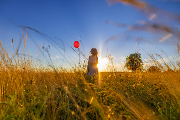 istock Girl playing with balloon while standing on grassy field against shining sun 1414489965