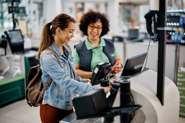 istock Young happy woman using self-service checkout with help of supermarket worker. 1414490236