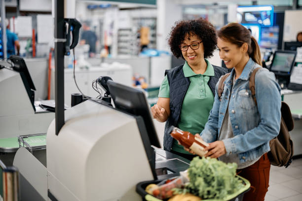 glückliche arbeiterin, die ihrer kundin bei der nutzung von selbstbedienungskassen im supermarkt hilft. - selbstbedienung stock-fotos und bilder